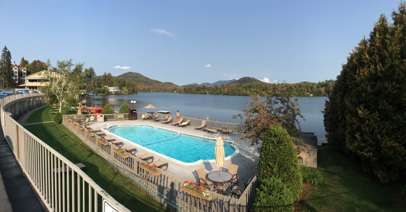 A swimming pool on a sunny day, overlooking a large lake with mountains in the background.