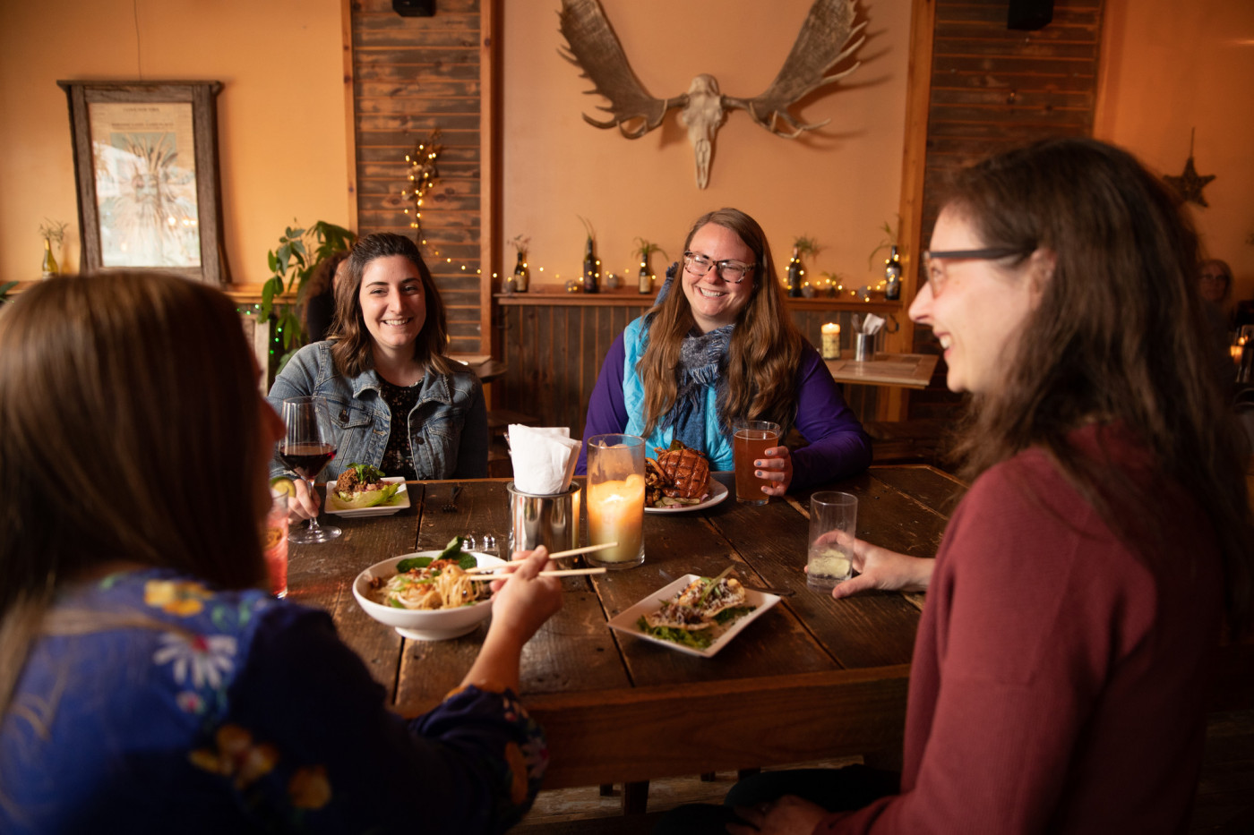 Four women sit ata  table in a rustic, light-filled restaurant with antlers on the wall.