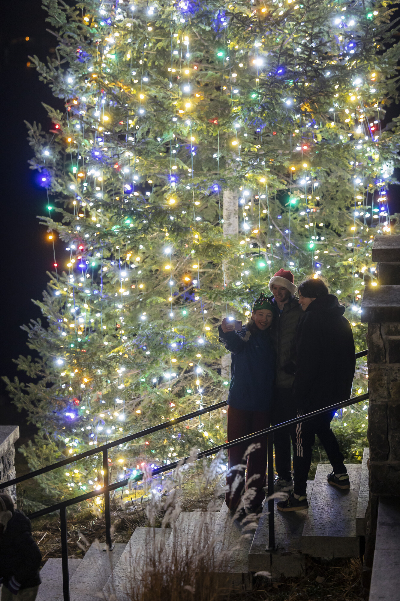 Two people taking a selfie in front of a lit Christmas tree