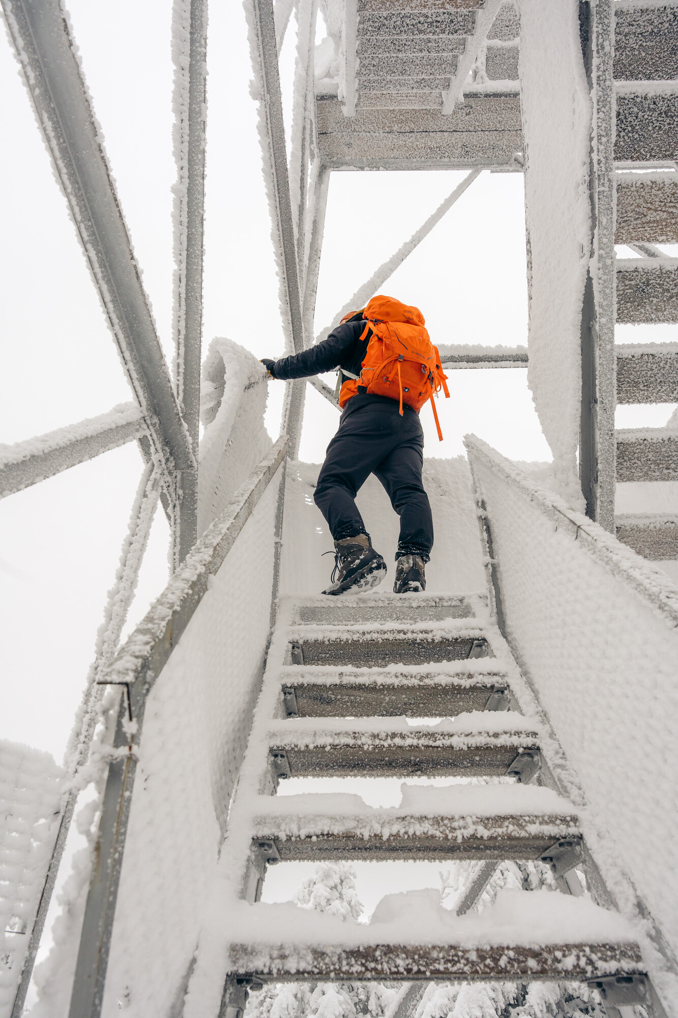 A snowshoer with an orange backpack on a firetower