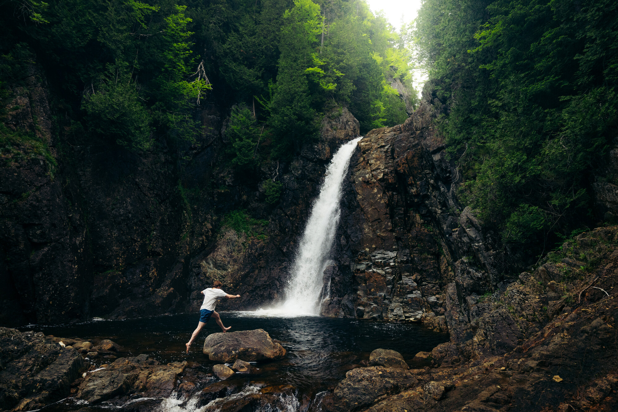 A man jumping rocks at the base of a waterfall