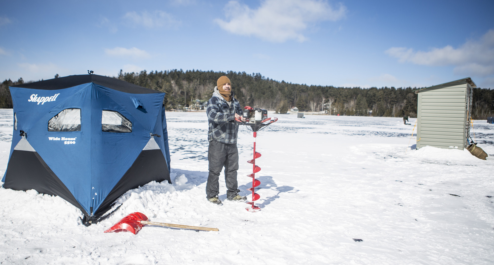 A man using an auger to drill a hole in the ice 