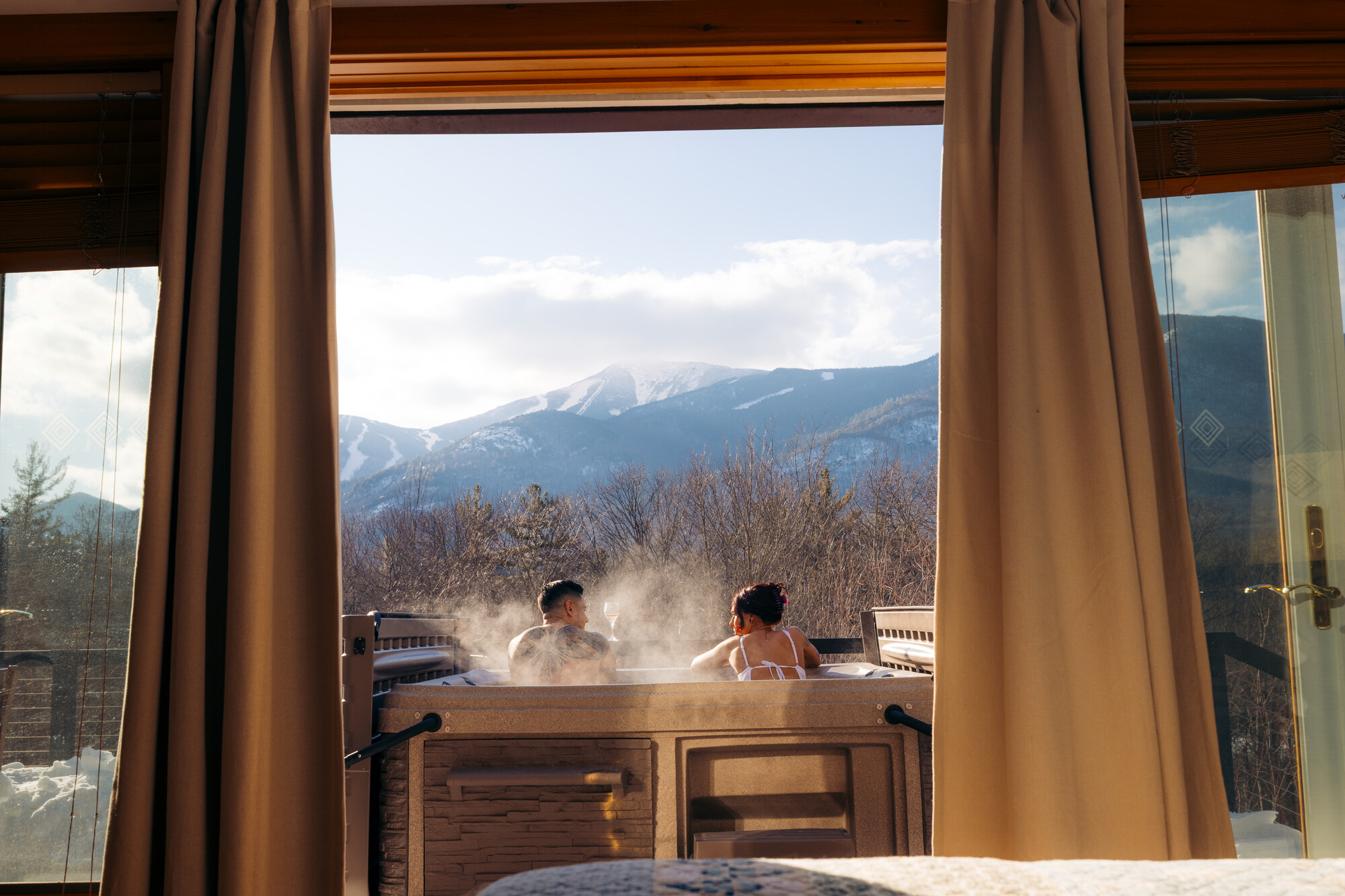 Two people in a hot tub in front of snow-covered peaks