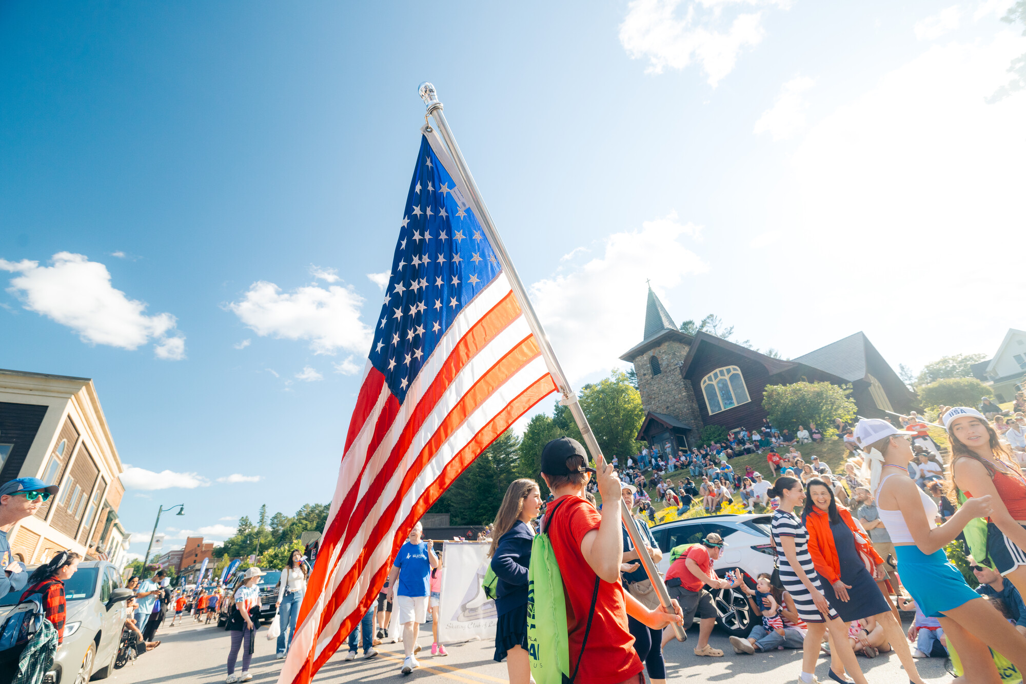 A teenager holds up a large American flag during a busy July 4 parade. 