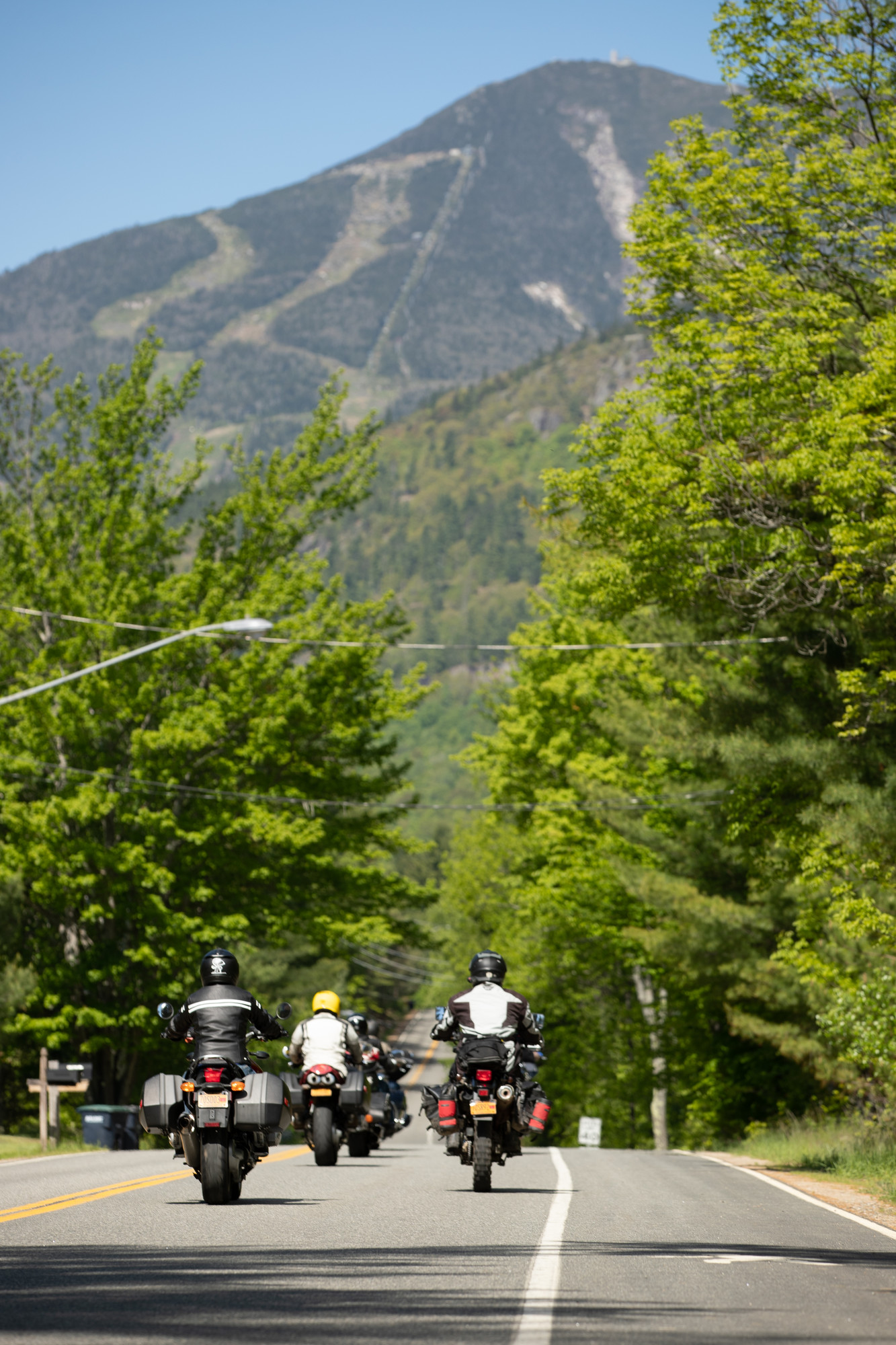 Three motorcycles travel down a road with a large mountain in the background. Ski trails can be seen on the mountainside.
