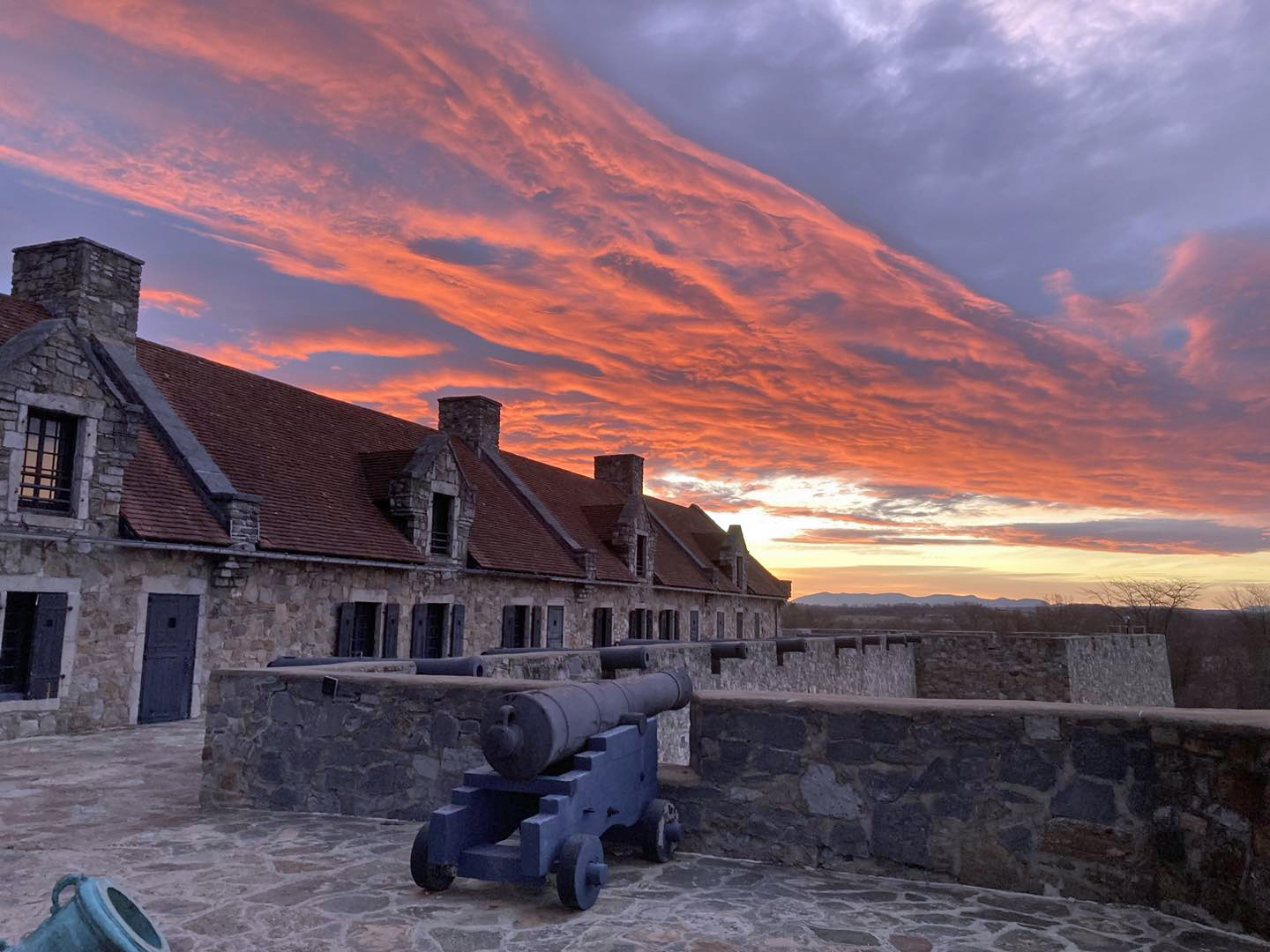 Sunrise over a stone fort. A cannon is in the foreground.