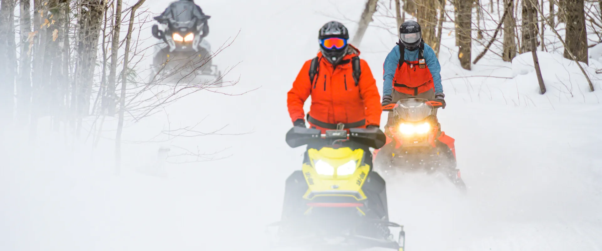 Three snowmobilers on a groomed trail kicking up snow
