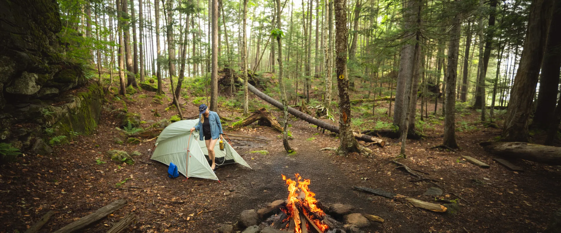 A backpacker by their tent next to a fire