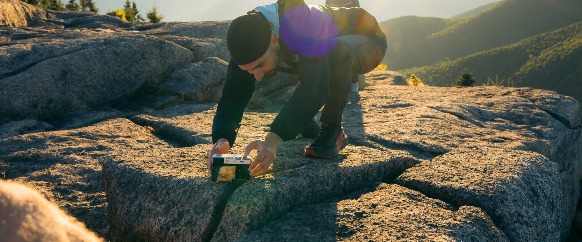 A man setting up his phone to take a photo on a mountain