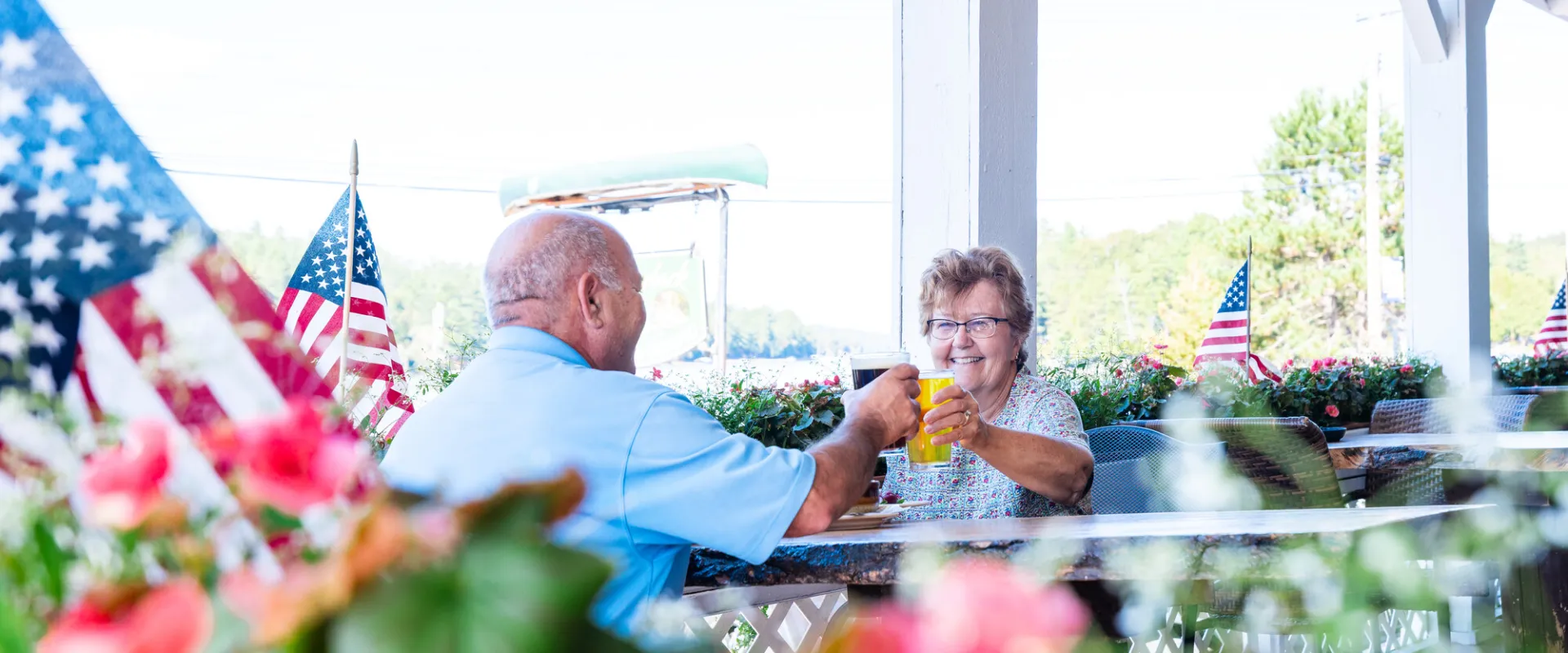 An older couple enjoying drinks by some flowers and flags