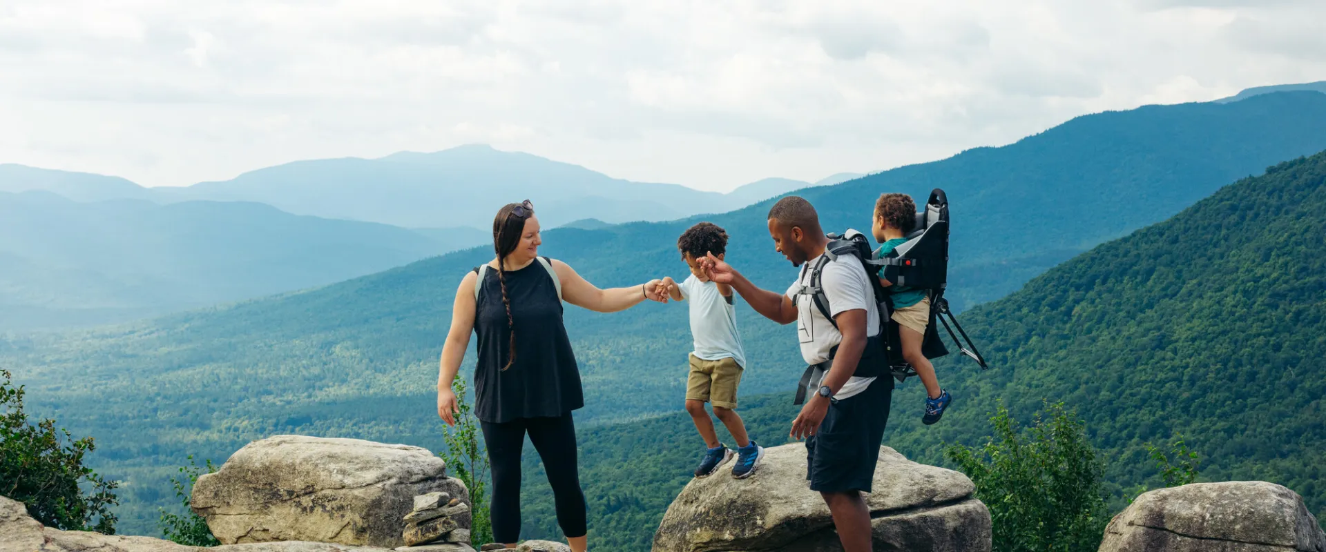 A man and woman play with their kids on top of a mountain. 