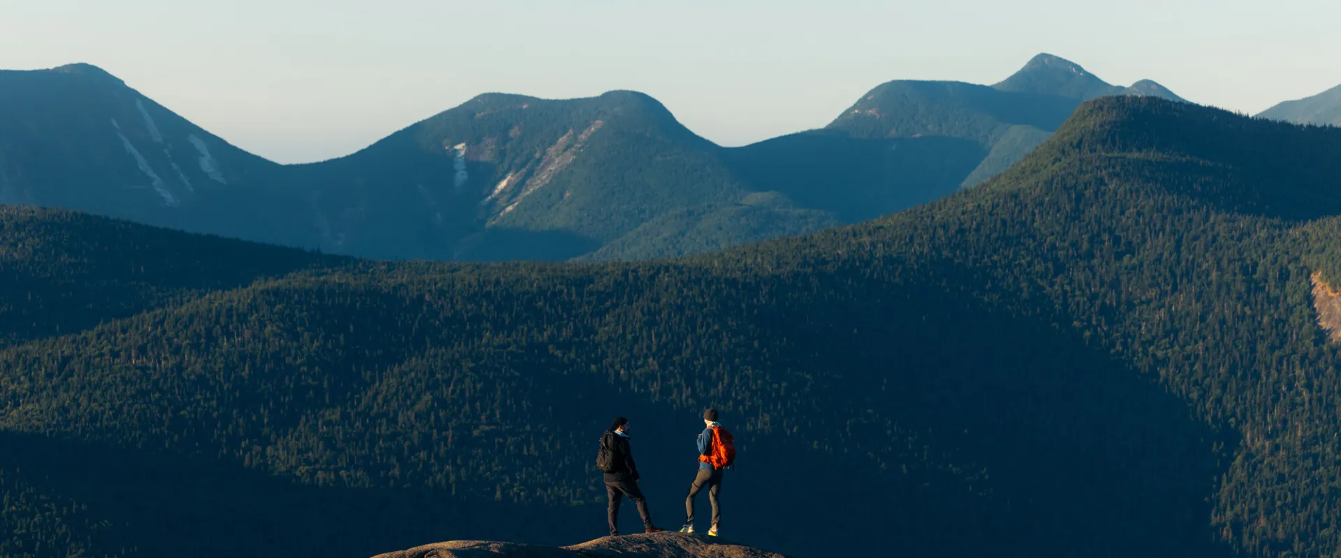 Two people stand looking out to a mountain range. 