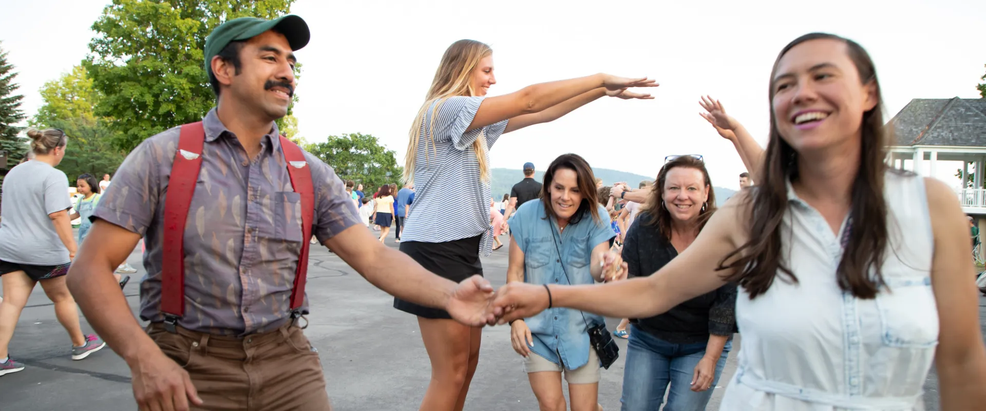 Adults and children smile as they dance outdoors on a summer evening.