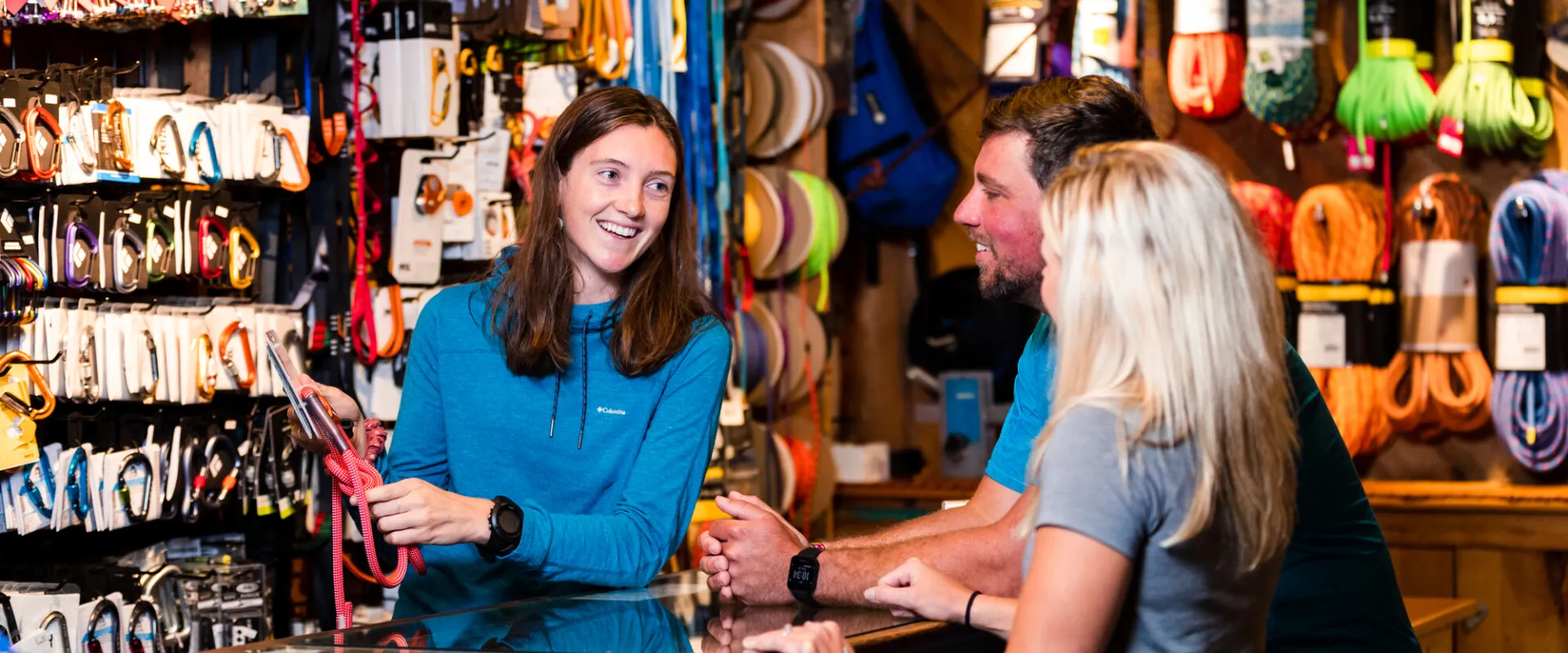 A woman shows a couple products at a hiking gear shop. 