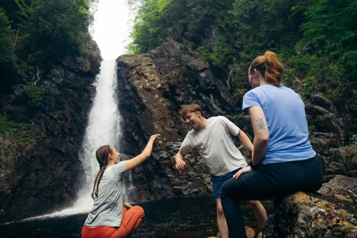 Three people hanging out by a tall waterfall