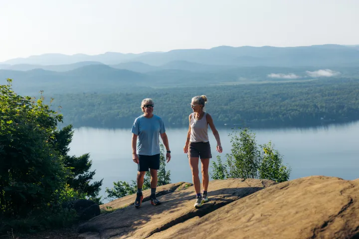 An older couple hiking on a summit cliff overlooking water