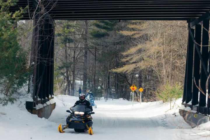 A snowmobiler going underneath a bridge