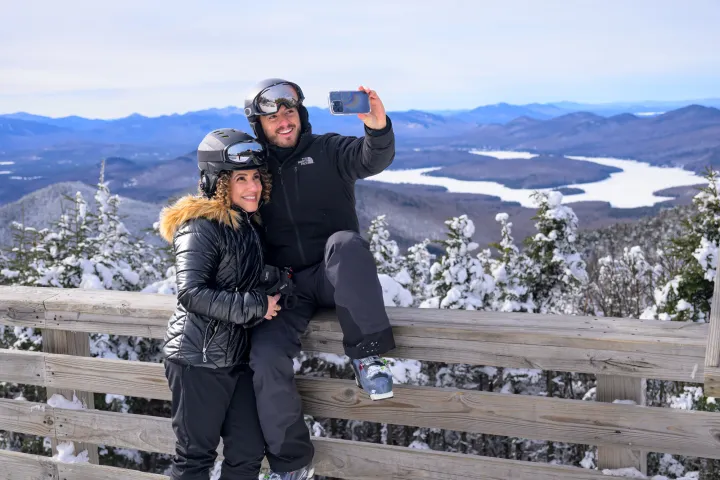 A man and woman in ski gear smile for a picture on top of a mountain. 
