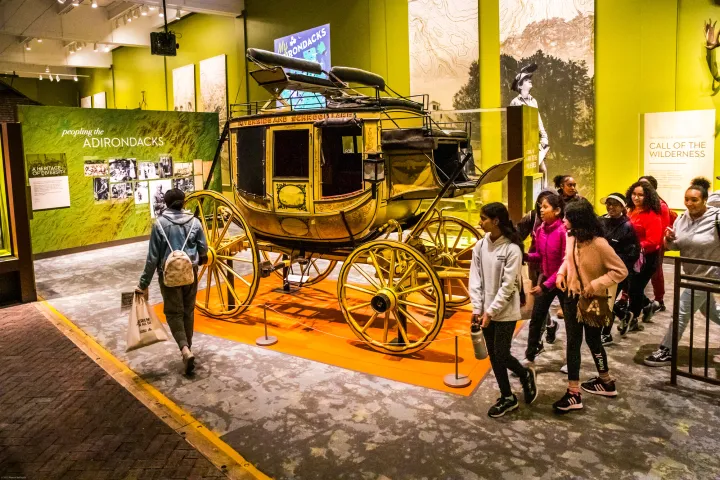A tour group walks around an old carriage in an art exhibit. 