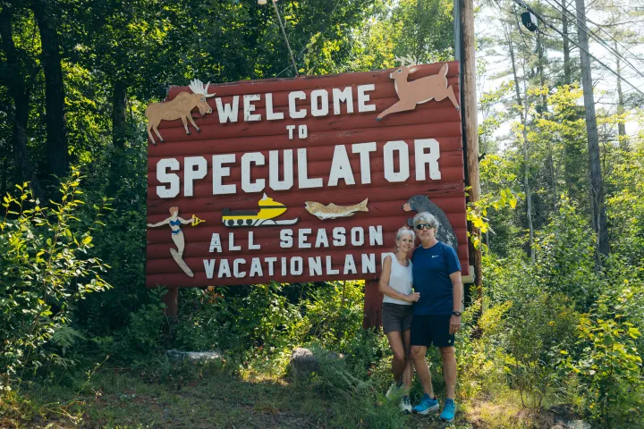 Two people in front of a Welcome to Speculator sign