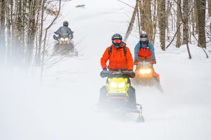 Three snowmobilers on a groomed trail kicking up snow