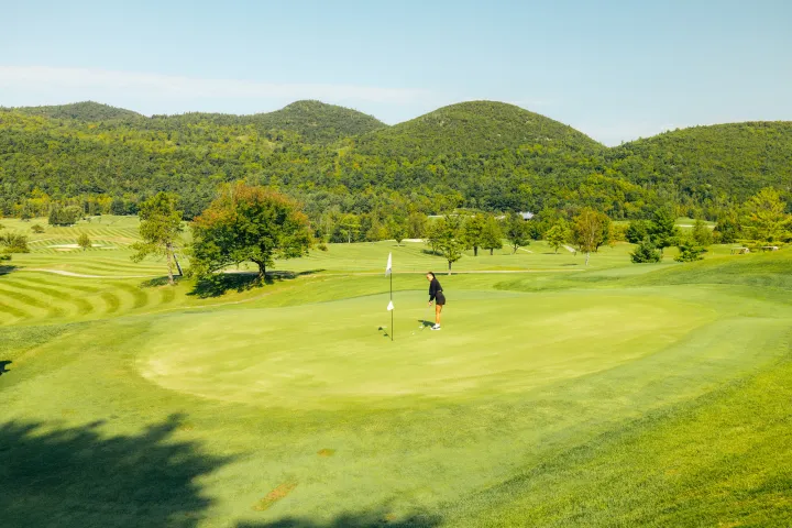 A woman putting on a green in the middle of mountains