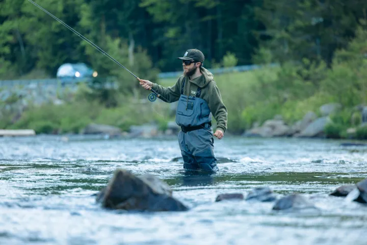 A fly fisher in a shallow river by a road
