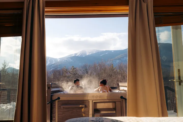 Two people in a hot tub in front of snow-covered peaks
