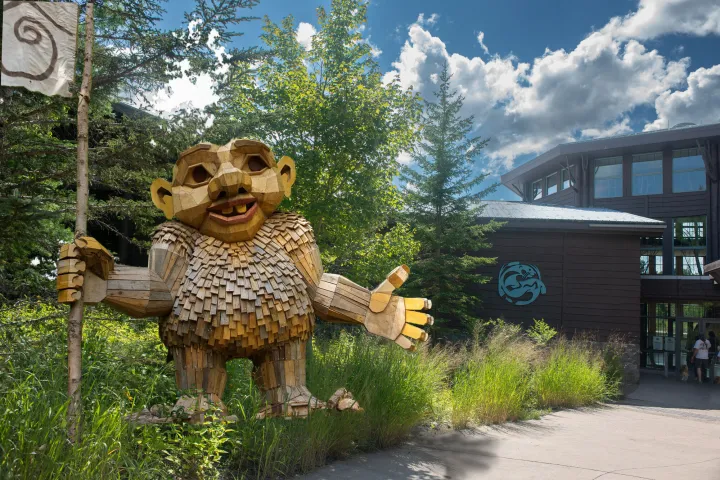 A large wooden troll stands next to a path at a nature center on a sunny day.