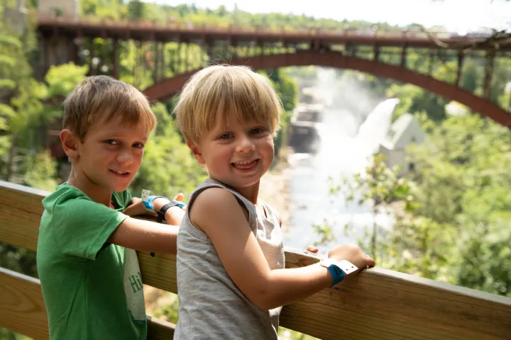 Two young boys pose for a picture in front of a bridge. 