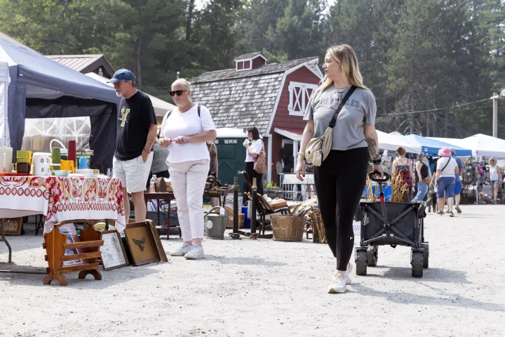 A woman strolls through an outdoor antique show. A miniature barn is in the background.