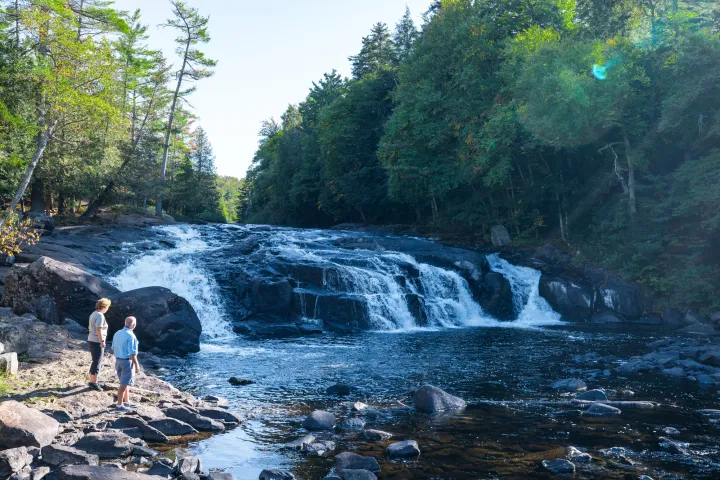 A man and woman look out to wide waterfalls. 