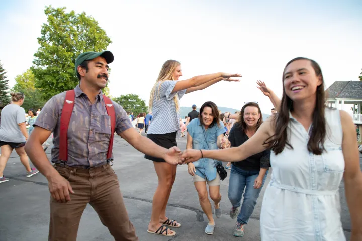 Adults and children smile as they dance outdoors on a summer evening.