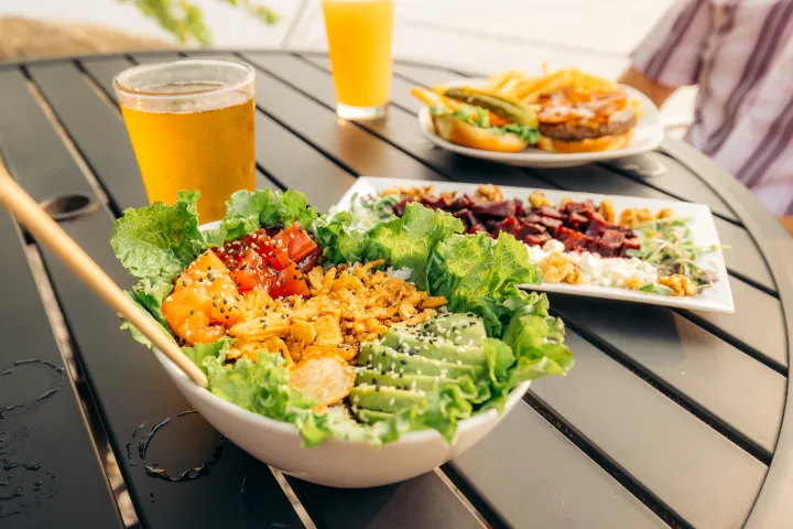 Close-up of three plates of food and two glasses of beer on a sunny outdoor restaurant table.