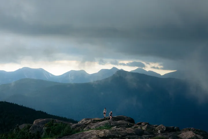 Two people walk along the top of a rocky mountain on an overcast day. 
