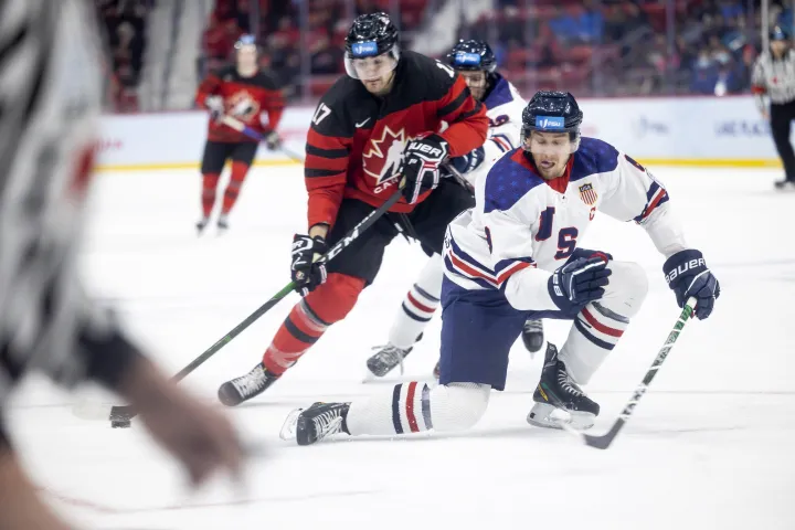 Two competing hockey players fight for control of the puck on an indoor rink.