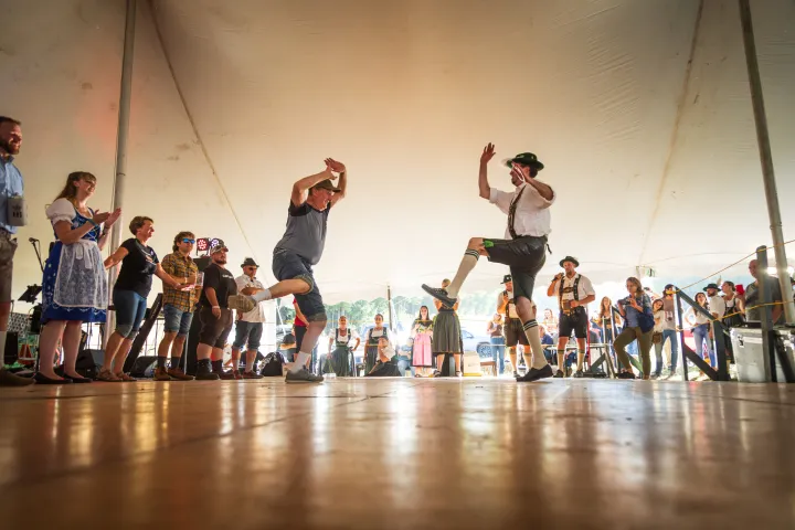 Dancers in Bavarian costumes dance under a large event tent.
