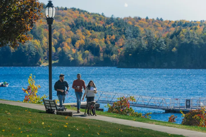 Three adults walk on a lakeside path on a sunny fall day.