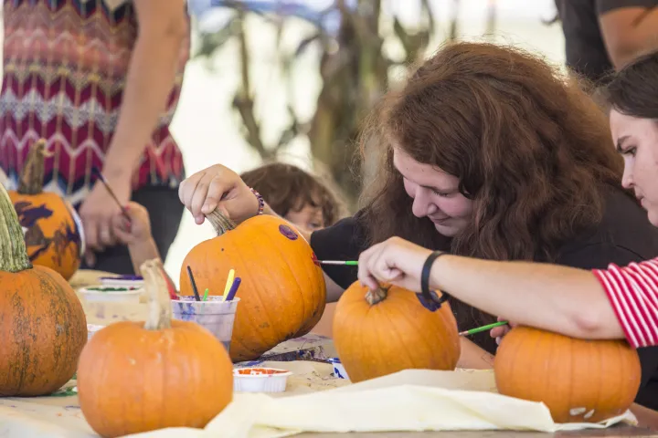 Children paint pumpkins at a fall festival.
