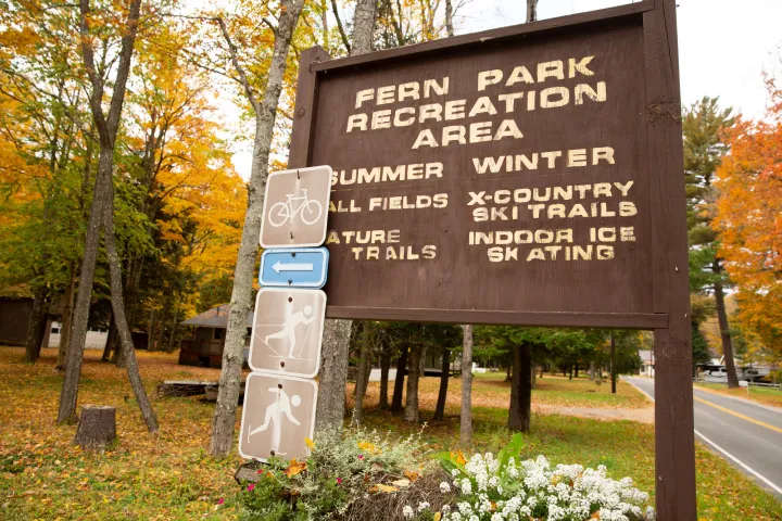 A large wooden sign to a recreation area amid fall foliage in a small town.