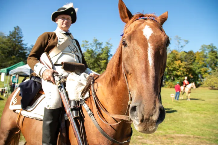 A man in the costume of a Revolutionary War soldier atop a brown and white horse.