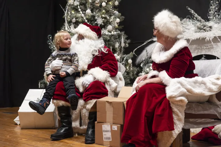 Santa Claus and Mrs. Claus sit in fur-trimmed chairs next to a Christmas tree.