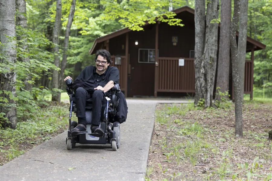 A person in a wheelchair near a rustic campground bathroom