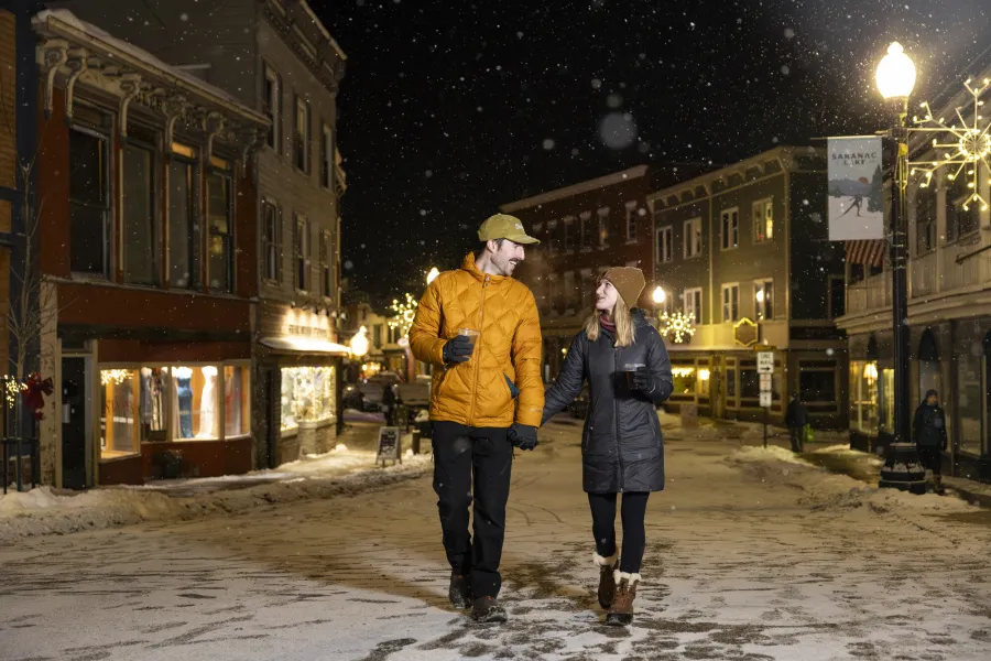 Two people walking down snowy Main Street in Saranac Lake