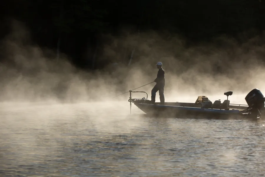 A bass fisher on a boat in the morning mist