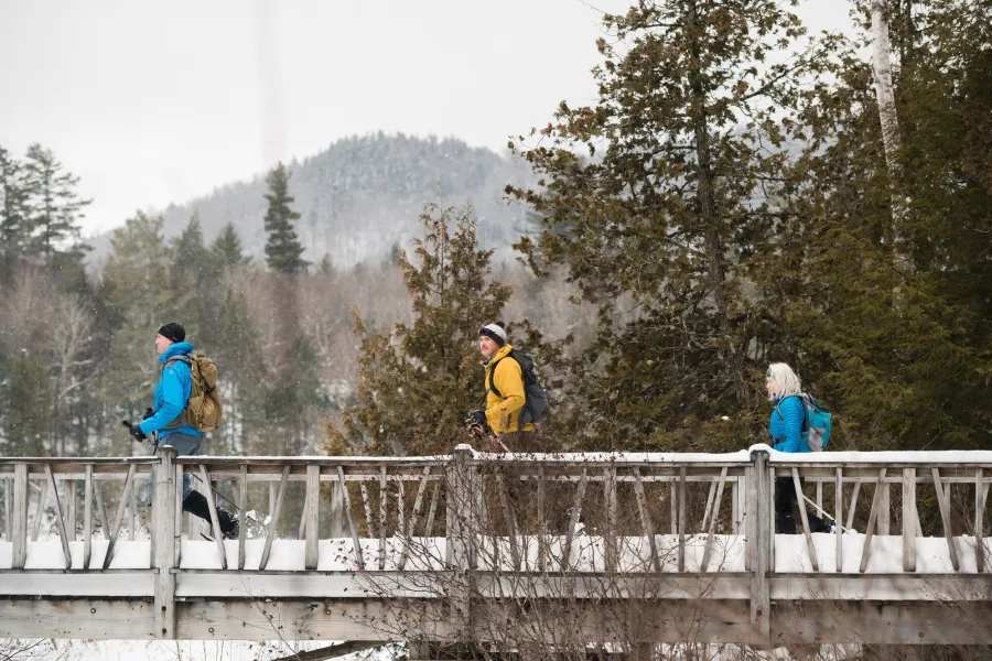 Snowshoers walking over a wooden walk bridge