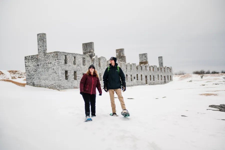 Two people snowshoeing at the ruins of a fort
