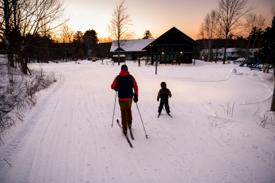 A father and kid xc skiing at dusk.