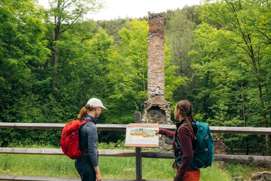 Two people looking at an interpretive sign in front of house ruins