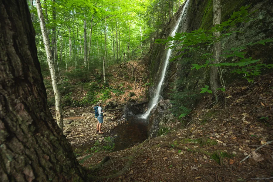 A solo hiker looking at a tall and narrow waterfall